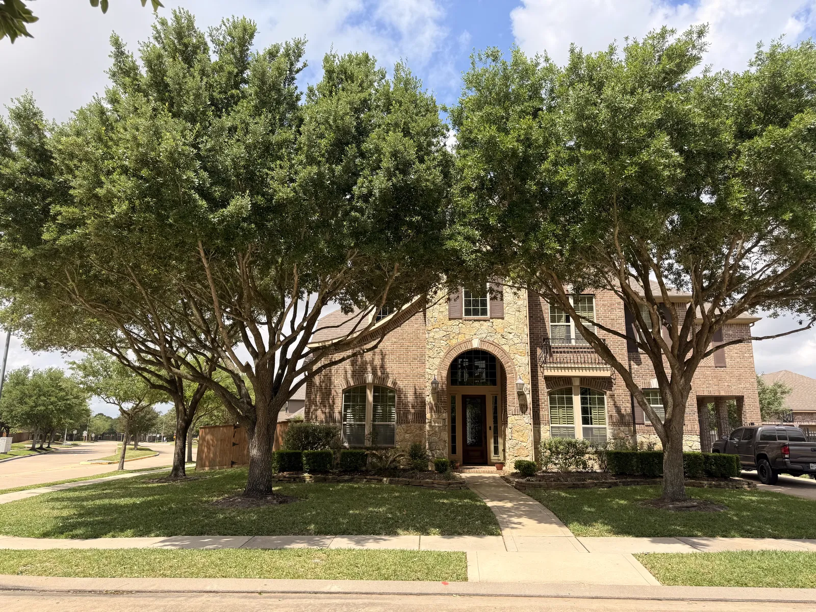 Brick estate after tree trimming — lifted canopies, home fully visible
