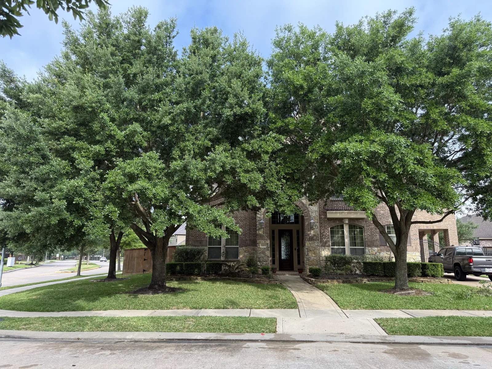 Brick estate before tree trimming — dense low canopies hiding the home